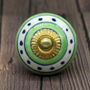 Könnte beinhalten: Grüner und weißer Keramik-Knopf mit goldener Mitte und blauen Punkten.