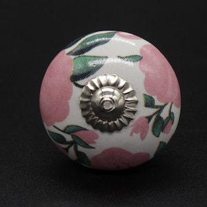 May include: A white ceramic knob with a pink and green floral design. The knob has a silver metal center.