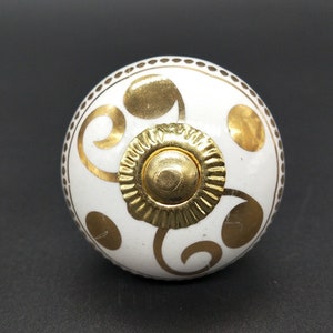 以下が含まれることがあります： 金色の渦巻き模様と金色のセンターが付いた白いセラミック製のノブ。ノブは点線の縁取りがされています。