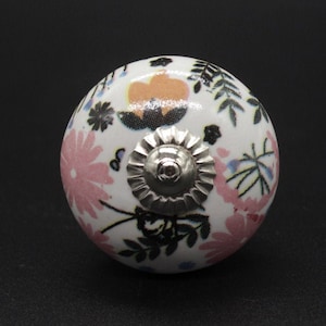 Op de afbeelding: Een witte keramische knop met een bloemenpatroon in roze, oranje, zwart en blauw. De knop heeft een zilveren metalen basis.