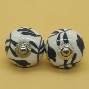 May include: Two white ceramic cabinet knobs with a black floral design. The knobs have a silver metal base.