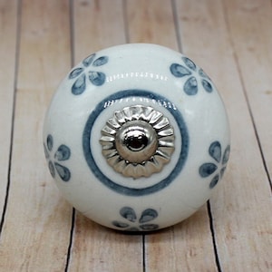 Può includere: Pomo in ceramica bianca con un motivo floreale blu e un centro in metallo argentato. Il pomo è rotondo e ha una superficie liscia.