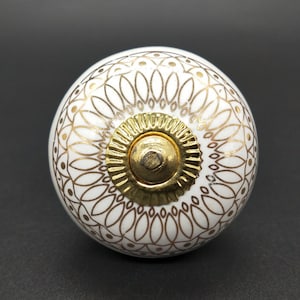 Peut inclure: Bouton de porte en céramique blanche avec un motif géométrique doré. Le bouton a un centre doré surélevé.