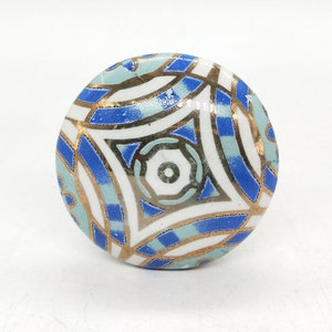 May include: A round ceramic knob with a blue, white and gold geometric pattern. The knob has a smooth, glossy finish.