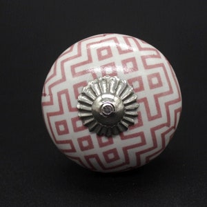 Könnte beinhalten: Ein weißer Keramik-Knopf mit einem rosafarbenen geometrischen Muster und einem silbernen Metallakzent.