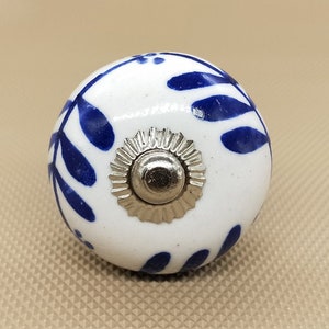 May include: White ceramic knob with a blue floral design and a silver metal center.