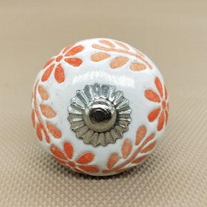 May include: White ceramic knob with a floral design in shades of orange. The knob has a silver metal center.