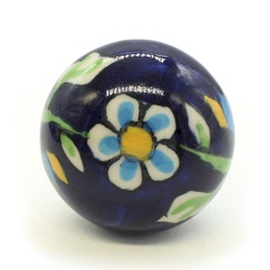 Puede incluir: Un pomo de cerámica azul con un diseño de flor blanca y azul. La flor tiene un centro amarillo y hojas verdes.