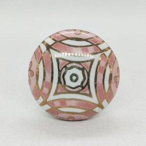 Op de afbeelding: Een ronde keramische knop met een geometrisch patroon in roze en wit en gouden accenten.