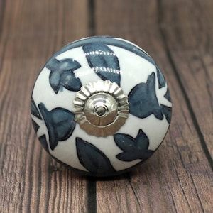 May include: A white ceramic knob with a blue floral pattern and a silver metal center. The knob is round and has a smooth surface.