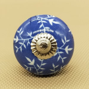 Może przedstawiać: Niebieski ceramiczny gałka z białym wzorem kwiatowym i srebrnym metalowym środkiem.