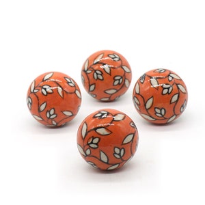 May include: Four orange ceramic spheres with a white and black floral design.