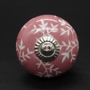 May include: A pink ceramic knob with a white leaf pattern and a silver metal center.