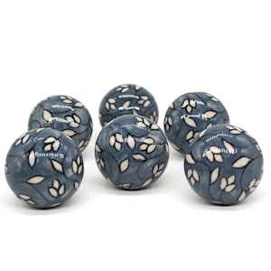 Peut inclure: Six boutons en céramique bleus avec un motif floral blanc. Les boutons sont ronds et ont une finition brillante.