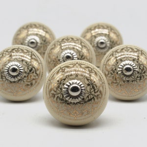 May include: Six off-white ceramic cabinet knobs with a silver center and gold filigree design.