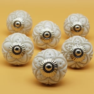 May include: Six white ceramic cabinet knobs with a floral design and gold accents. The knobs are round and have a raised floral pattern.