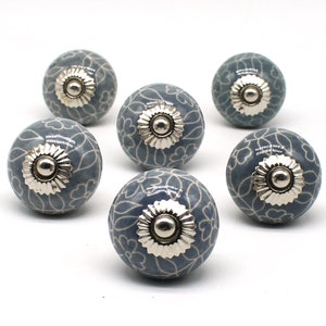May include: Six gray ceramic cabinet knobs with a white floral pattern and silver metal accents.