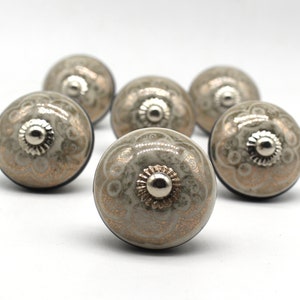May include: Set of six grey ceramic cabinet knobs with a silver metal accent. Each knob features a decorative floral pattern with gold accents.