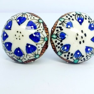 May include: Two round ceramic knobs with a white background and a blue and brown floral design.