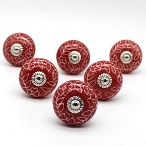 May include: Six red ceramic knobs with white floral designs and silver accents.