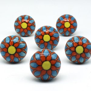 Könnte beinhalten: Sechs Keramik-Knöpfe mit blauem Hintergrund und rotem Blumendesign mit gelber Mitte.