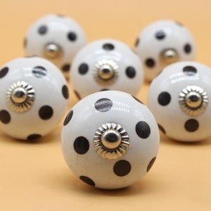 Puede incluir: Seis pomos de armario de cerámica blanca con lunares negros y detalles plateados.