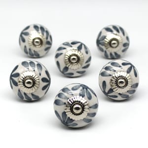 Peut inclure: Six boutons en céramique blanche avec un motif floral bleu et des accents argentés. Les boutons sont ronds et ont une finition lisse.
