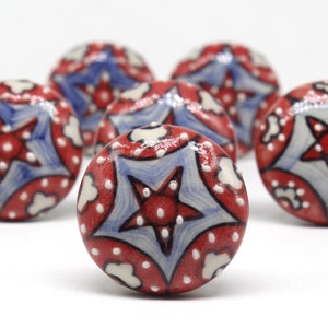 May include: Six red, white and blue ceramic drawer knobs with a star design. The knobs have a glossy finish.
