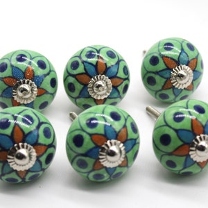 Può includere: Set di sei pomelli per armadi in ceramica verde con un design floreale in tonalità di blu, arancio e bianco. Ogni pomello ha una base in metallo argentato.