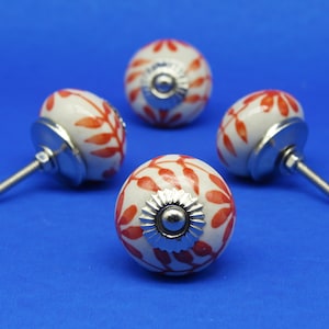 May include: Four white ceramic cabinet knobs with red leaf designs and silver accents.