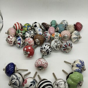 May include: Assortment of colourful ceramic cabinet knobs with various floral and geometric patterns. The knobs have a silver metal base and are perfect for adding a touch of vintage charm to any home decor.
