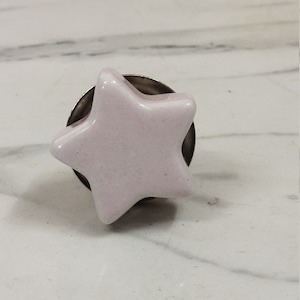 Könnte beinhalten: Ein hellrosa Keramik-Knopf in Sternform mit silberner Basis.