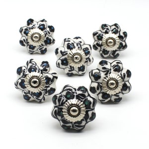 Könnte beinhalten: Sechs weiße Keramik-Schrankknöpfe mit einem schwarzen und blauen Blumenmuster. Jeder Knopf hat eine silberne Metallbasis.
