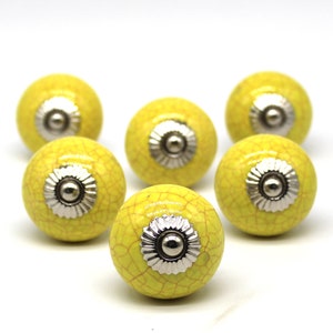 Może przedstawiać: Sześć żółtych ceramicznych gałek do szafek z srebrnym metalowym akcentem. Gałki mają pęknięte wykończenie.