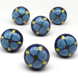 May include: Six blue and yellow ceramic cabinet knobs with a floral design. Each knob features a blue flower with a yellow center and yellow accents around the edges.
