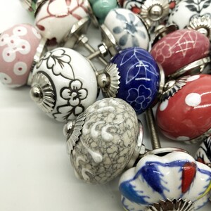 May include: A collection of ceramic drawer knobs featuring a variety of floral and geometric patterns. The knobs are in shades of white, blue, red, green, and pink. Each knob has a silver metal base.