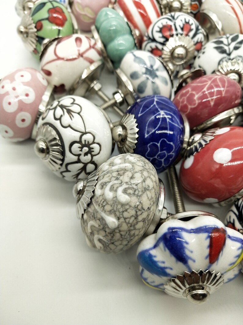 May include: A collection of ceramic drawer knobs featuring a variety of floral and geometric patterns. The knobs are in shades of white, blue, red, green, and pink. Each knob has a silver metal base.