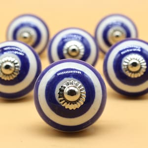 May include: Set of six blue and white ceramic knobs with silver accents. Each knob features a circular design with alternating blue and white stripes.