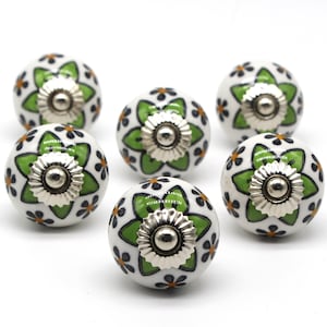 以下が含まれることがあります： 緑とオレンジの花柄が施された白いセラミック製のノブが6個。各ノブには銀色の金属ベースが付いています。