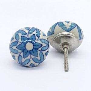May include: Two blue and white ceramic cabinet knobs with a floral design. The knobs have a silver metal screw.