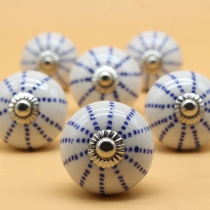 May include: Six white ceramic cabinet knobs with a blue and white geometric pattern. The knobs have a silver metal accent in the center.