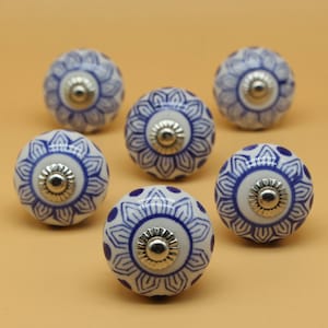 May include: Six white ceramic cabinet knobs with blue floral patterns and silver-colored metal hardware. The knobs are round and have a detailed design, perfect for adding a decorative touch to furniture or cabinetry.
