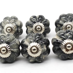 May include: Six grey and white ceramic cabinet knobs with a silver metal accent. The knobs have a marbled pattern and a slightly raised, rounded shape.
