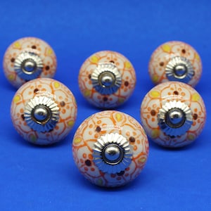 May include: Six decorative cabinet knobs with a floral design. The knobs are round, with a white base and orange, yellow, and brown floral patterns. Each knob has a silver-colored metal base and a central screw.