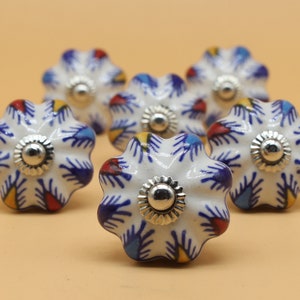 May include: Six white ceramic cabinet knobs with a blue, red, and yellow floral pattern. The knobs have a silver metal base.