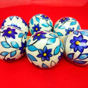 May include: Six white ceramic ornaments with blue and yellow floral designs. The ornaments are round and have a glossy finish.