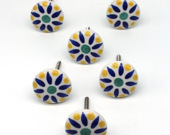 Op de afbeelding: Set van zes keramische ladeknopjes met een witte achtergrond en een blauw en geel bloemenontwerp. De knoppen hebben een zilveren schroef.