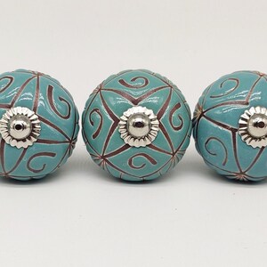 Pode incluir: Cinco botões de armário de cerâmica turquesa com um design de redemoinho marrom e detalhes prateados.