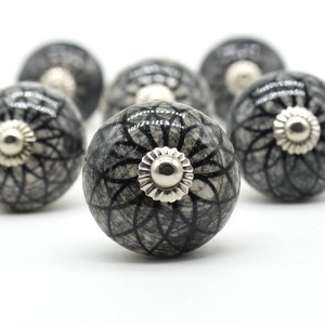 May include: A set of six gray ceramic cabinet knobs with a black floral design and silver accents.
