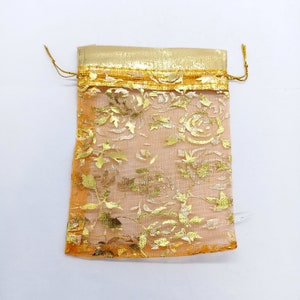 Puede incluir: Una pequeña bolsa de malla dorada y melocotón con un patrón floral. La bolsa tiene un cierre de cordón y es perfecta para pequeños regalos o favores.